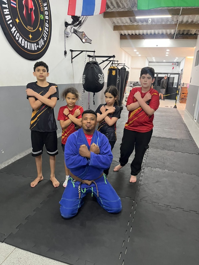 Prof. Kleiton de quimono azul e alunos da turma de Jiu-Jitsu perfilados no tatame da Equipe NT Fight